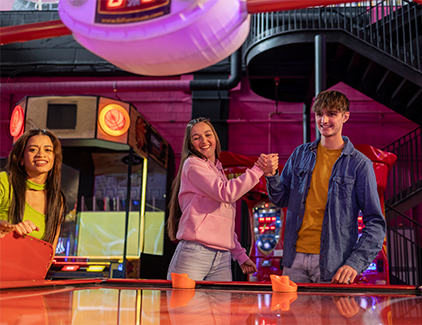 Group of young adults celebrating at an arcade air hockey table, representing high-traffic entertainment & hospitality venues for hassle-free ATM solutions.