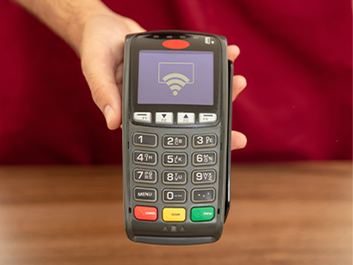 Hand holding Cashless POS terminal with contactless payment icon for retail or small business transactions.